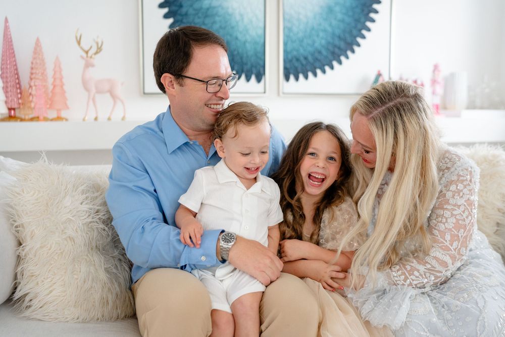 A family shares a joyful moment together on a white couch with decorative wall art featuring deer and geometric shapes.
