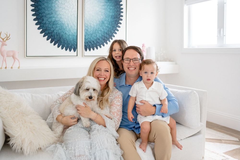 A family poses on their couch with their white fluffy dog in a modern living room with artistic wall decor.