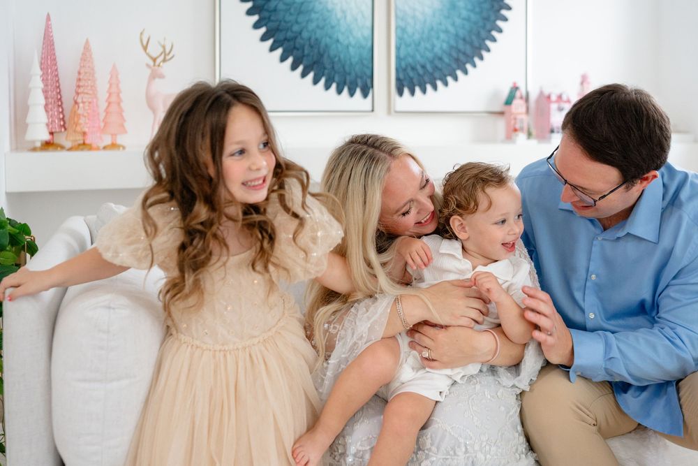 A family shares joyful moments together in a bright indoor setting with white decor and floral accents.