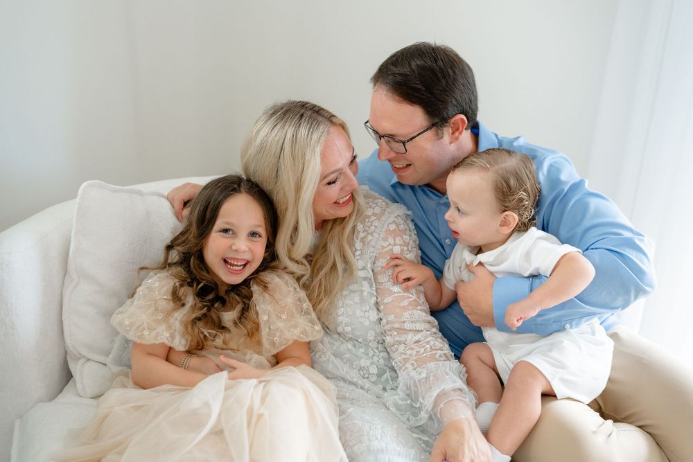 A family shares joyful moments together while relaxing on a white couch in a bright room.