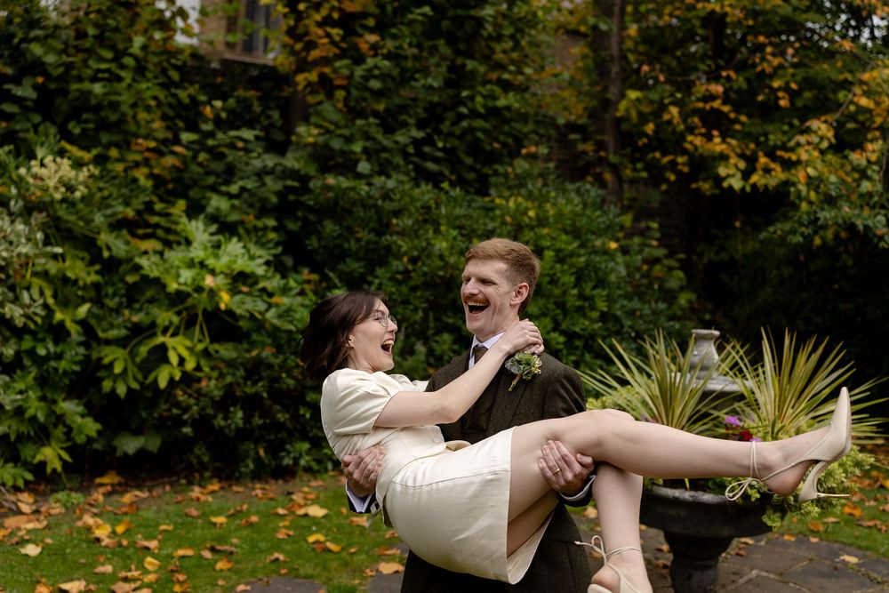 A couple performs playful dance moves in a lush garden setting with autumn leaves scattered on the ground.