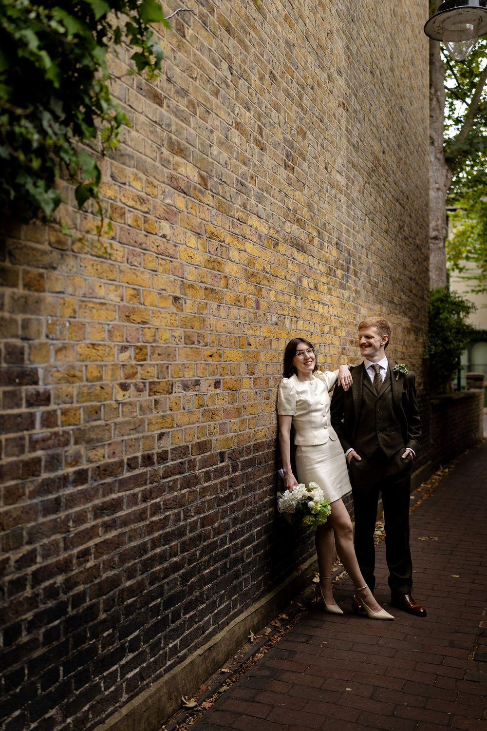 A couple poses along a brick wall in a sequence of romantic wedding photos showing playful interaction and movement.