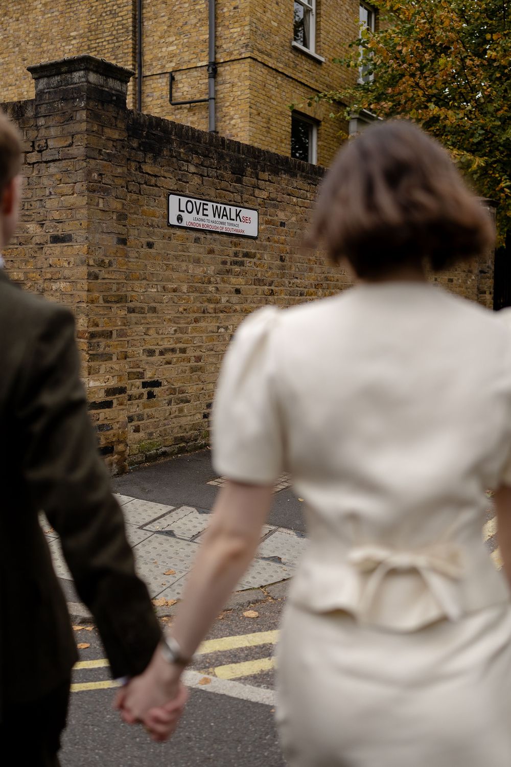A couple walking down a stone-lined street with a Love Walk street sign visible in the background.