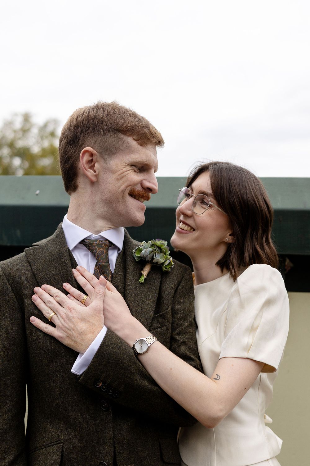 A joyful wedding couple shares a candid moment together outdoors, both wearing classic vintage-inspired attire.