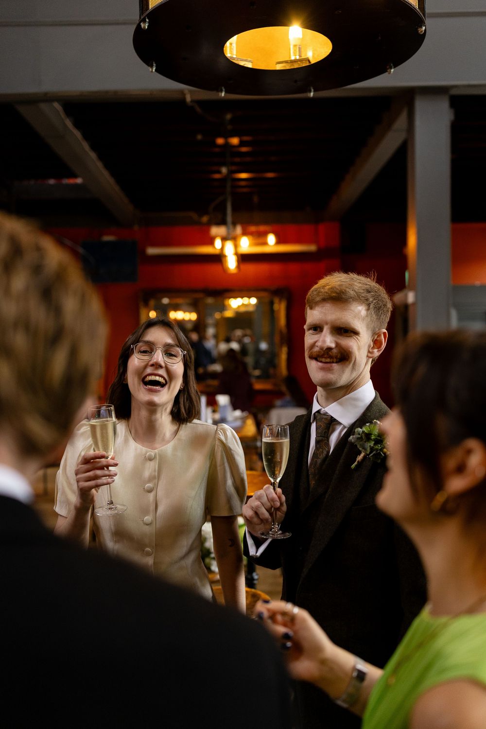 Guests raise champagne glasses during a celebration at a dimly lit bar with warm ambient lighting.