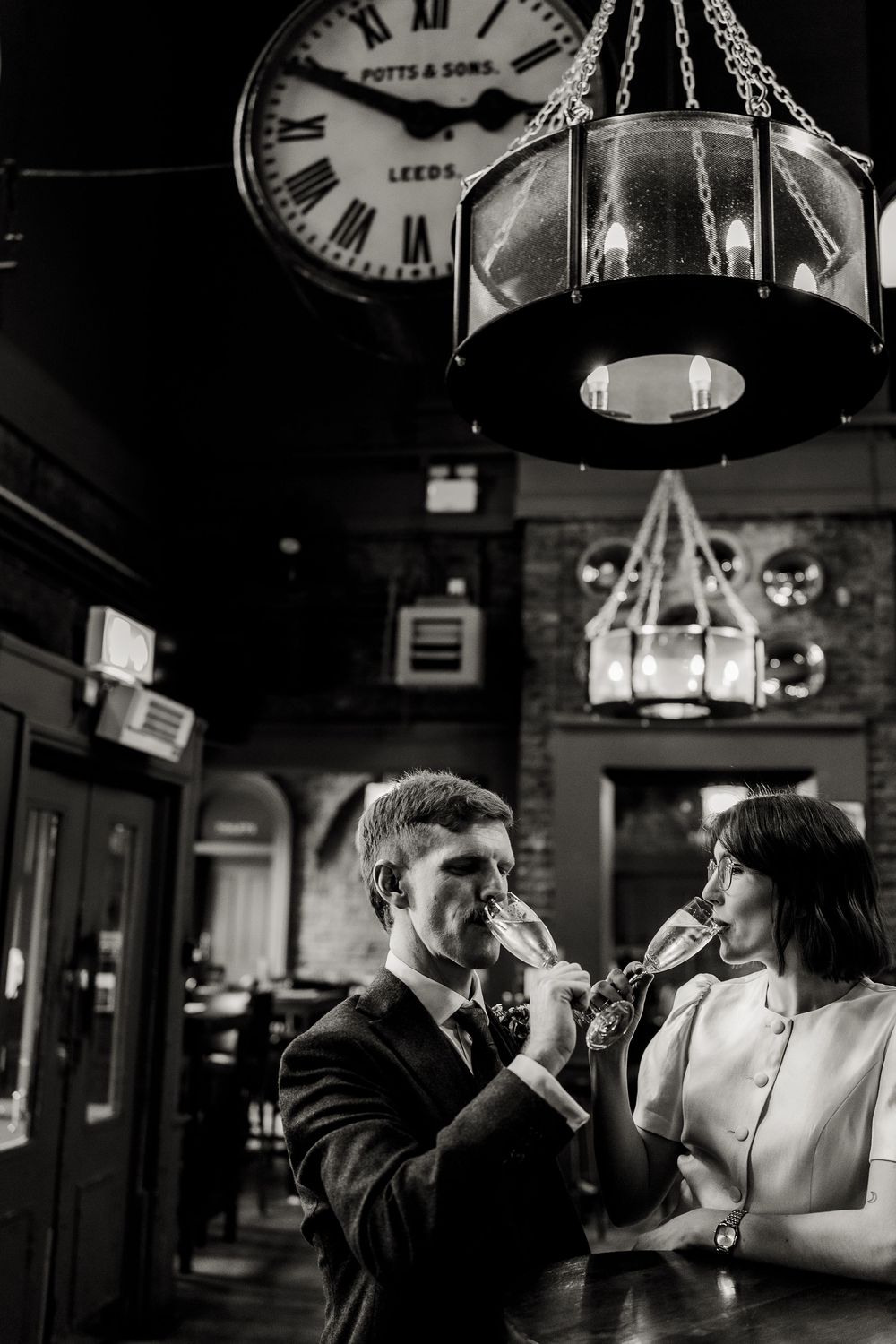 A couple shares a drink together at a bar with vintage clocks on the wall in a romantic setting.