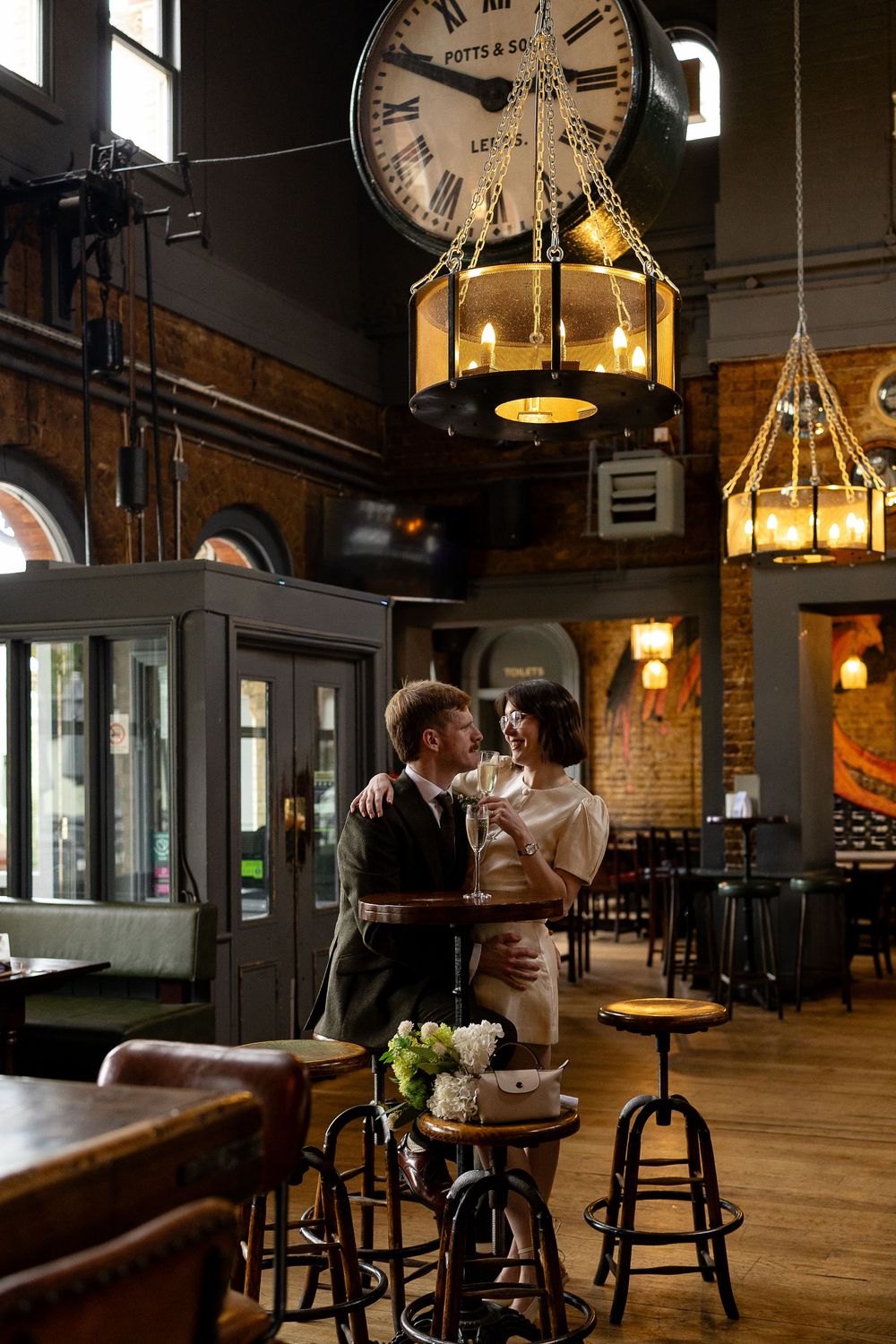 A dimly lit vintage pub interior with wooden bar stools and hanging lantern lights beneath a large clock.
