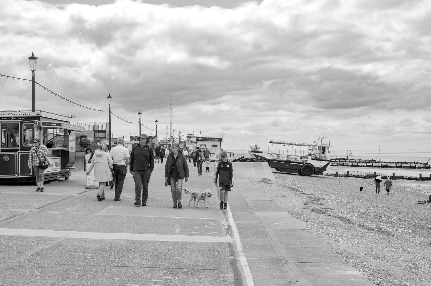 A series of black and white photographs showing people walking along a coastal boardwalk on a cloudy day.