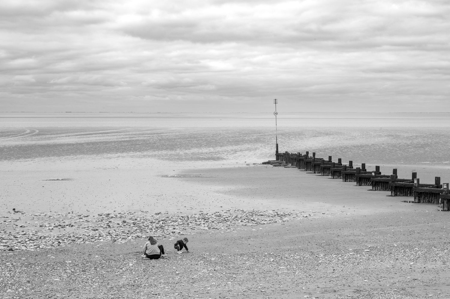 Minimalist black and white seascape showing wooden groynes extending into a misty ocean.