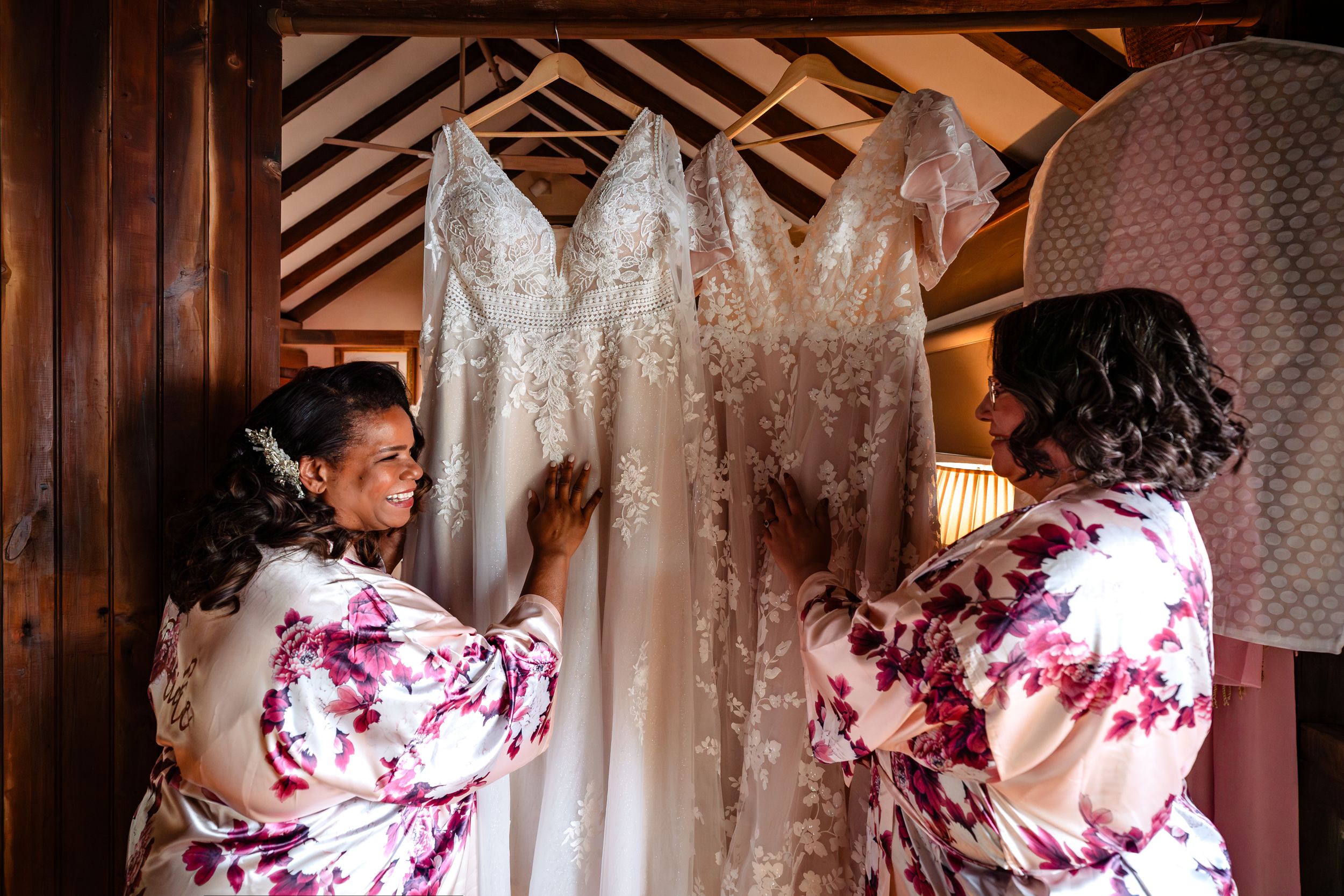 Wedding dress preparations with floral robes and white gowns hanging in a sunlit dressing room.