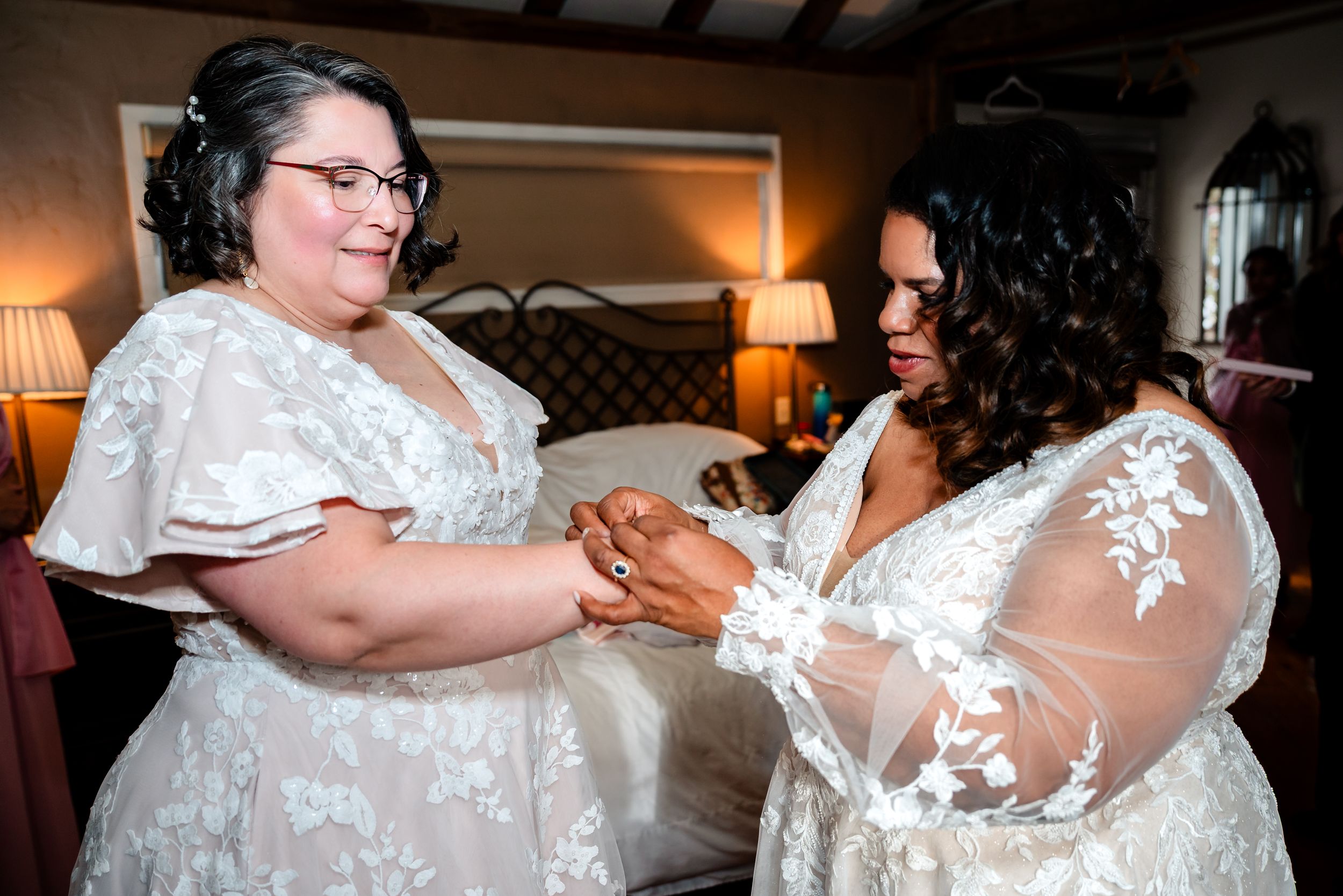 Wedding party members embrace in elegant white lace and floral dresses.