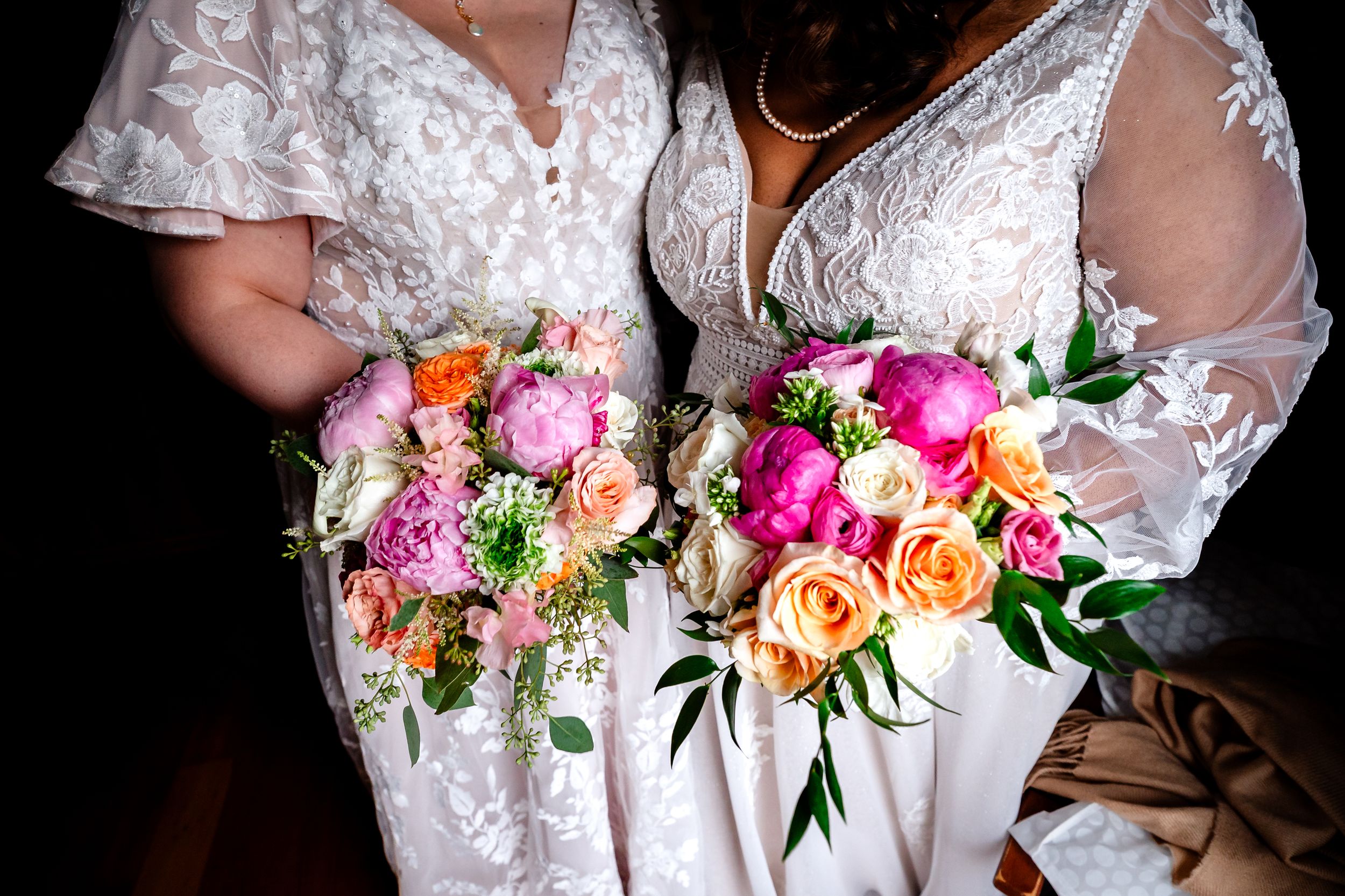 A vibrant pink and peach floral bouquet is held against a white lace dress.