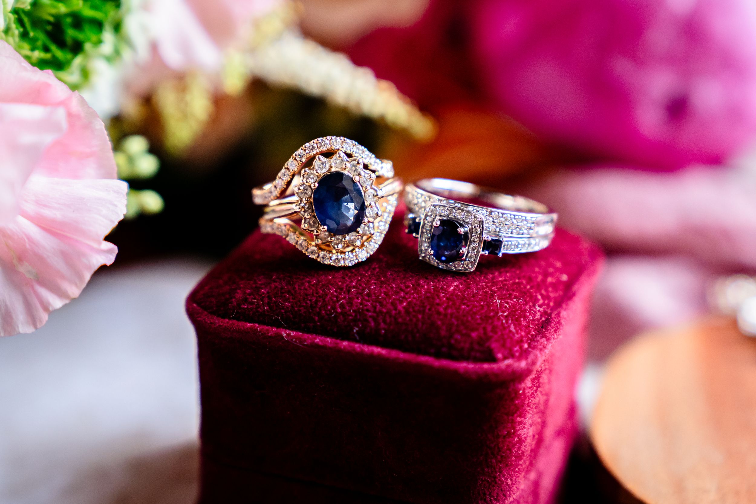 Close-up of elegant engagement rings on burgundy velvet cushion with pink floral accents.