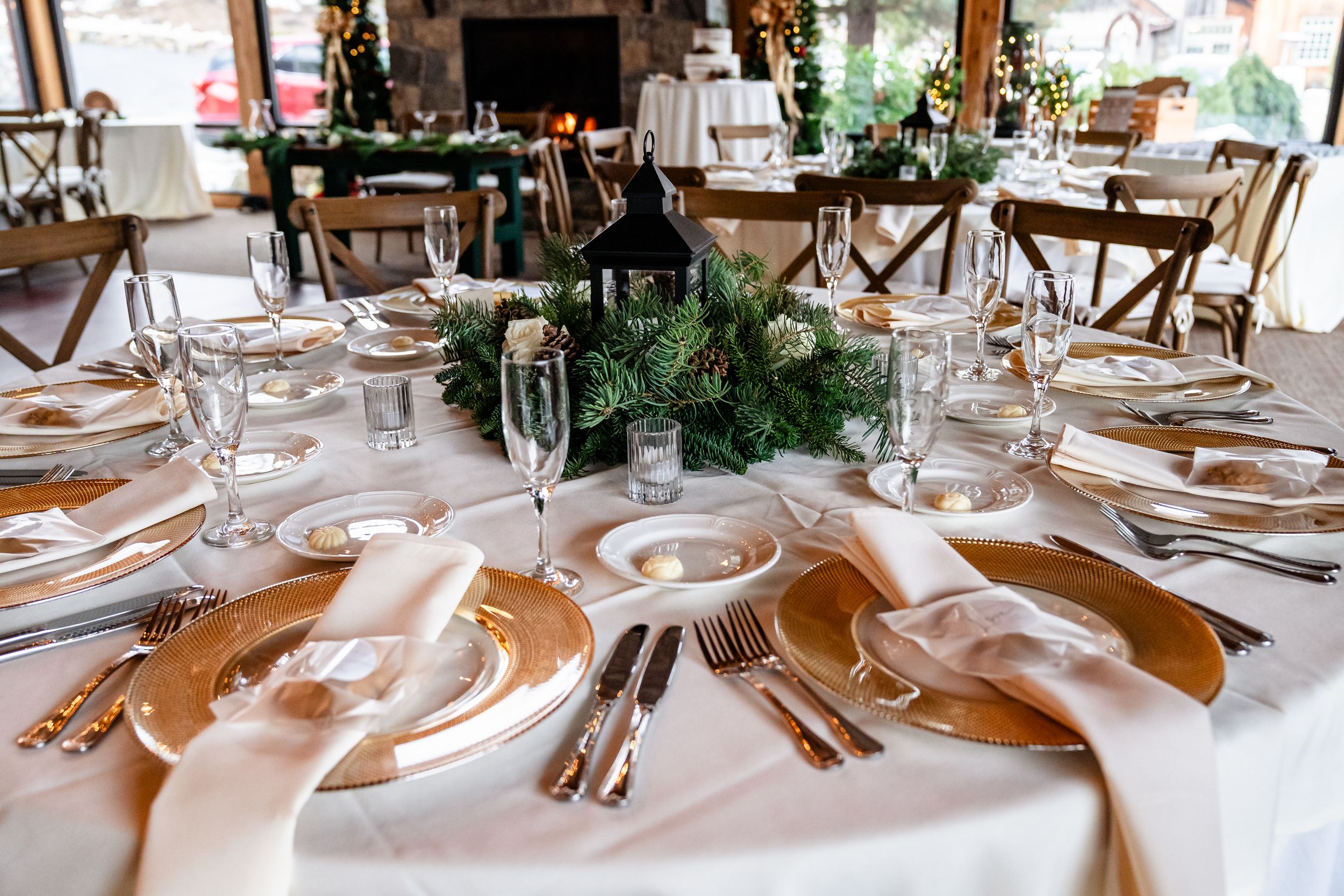 Elegant wedding reception table settings with white linens, glassware, and natural greenery decor in a bright venue.