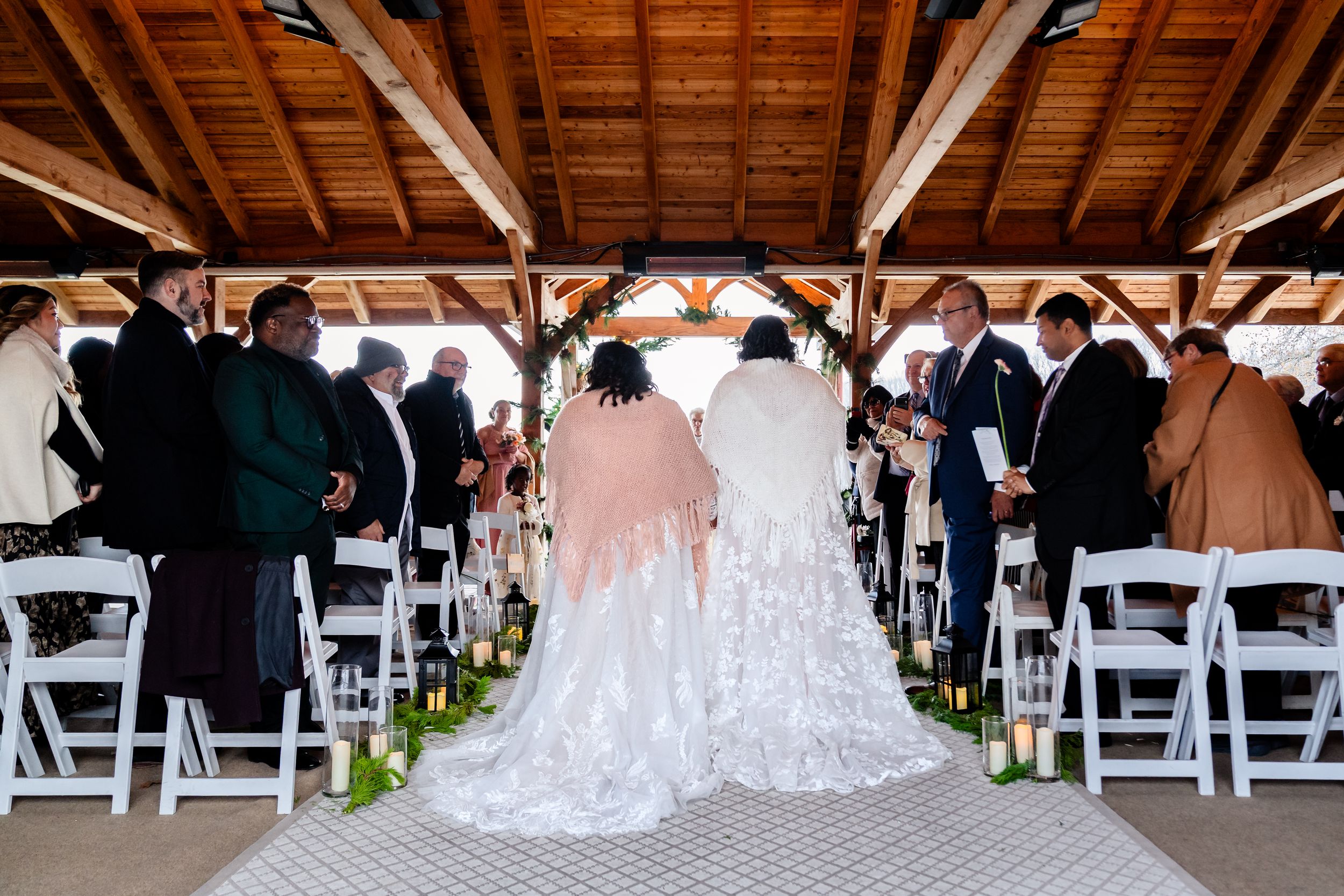 Two people in wedding attire stand at the altar during an indoor ceremony with wooden beams.