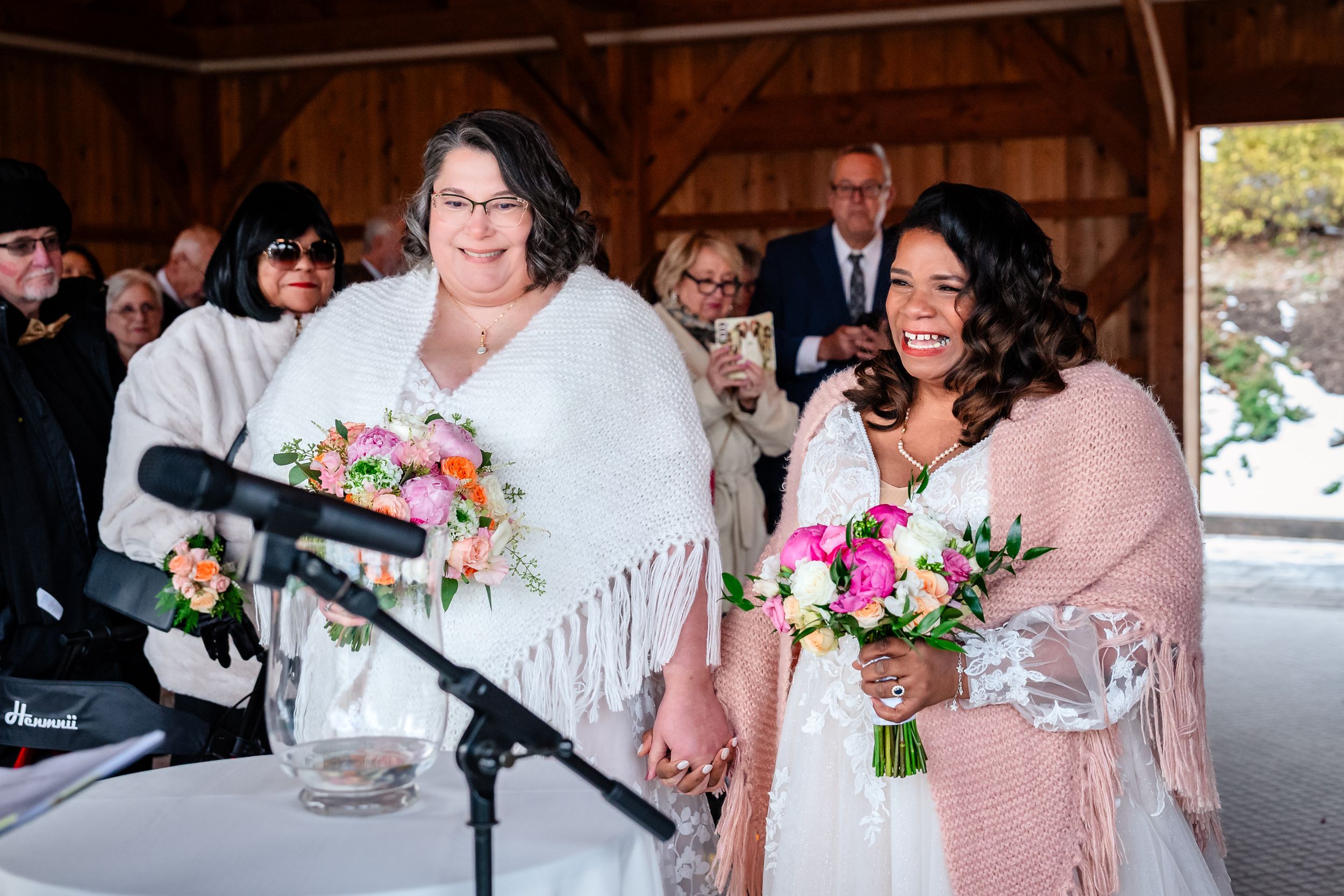 Wedding reception gathering in a rustic barn venue with floral arrangements and pink accents.