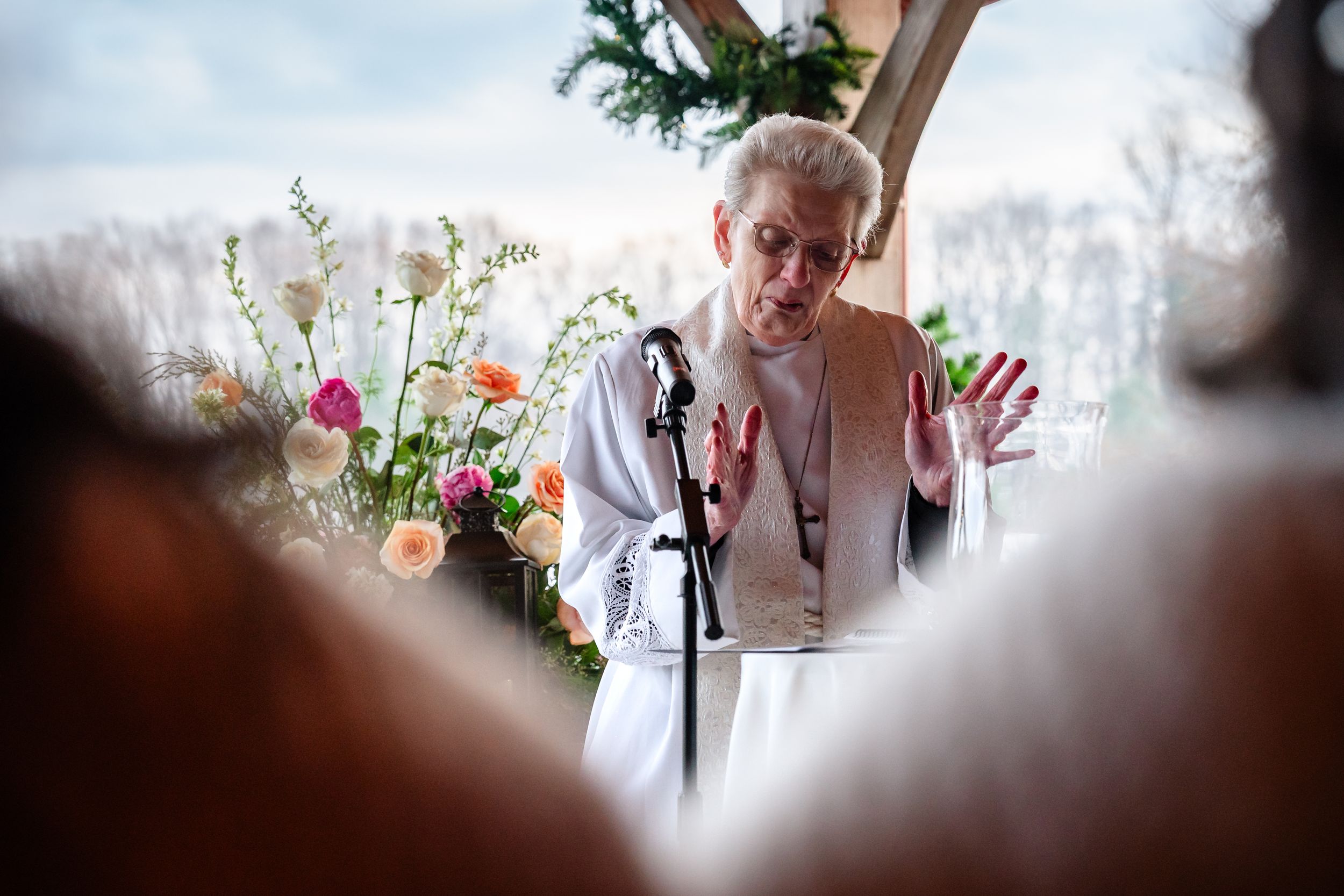 A speaker gestures animatedly while giving a speech at a wedding ceremony with floral decorations.