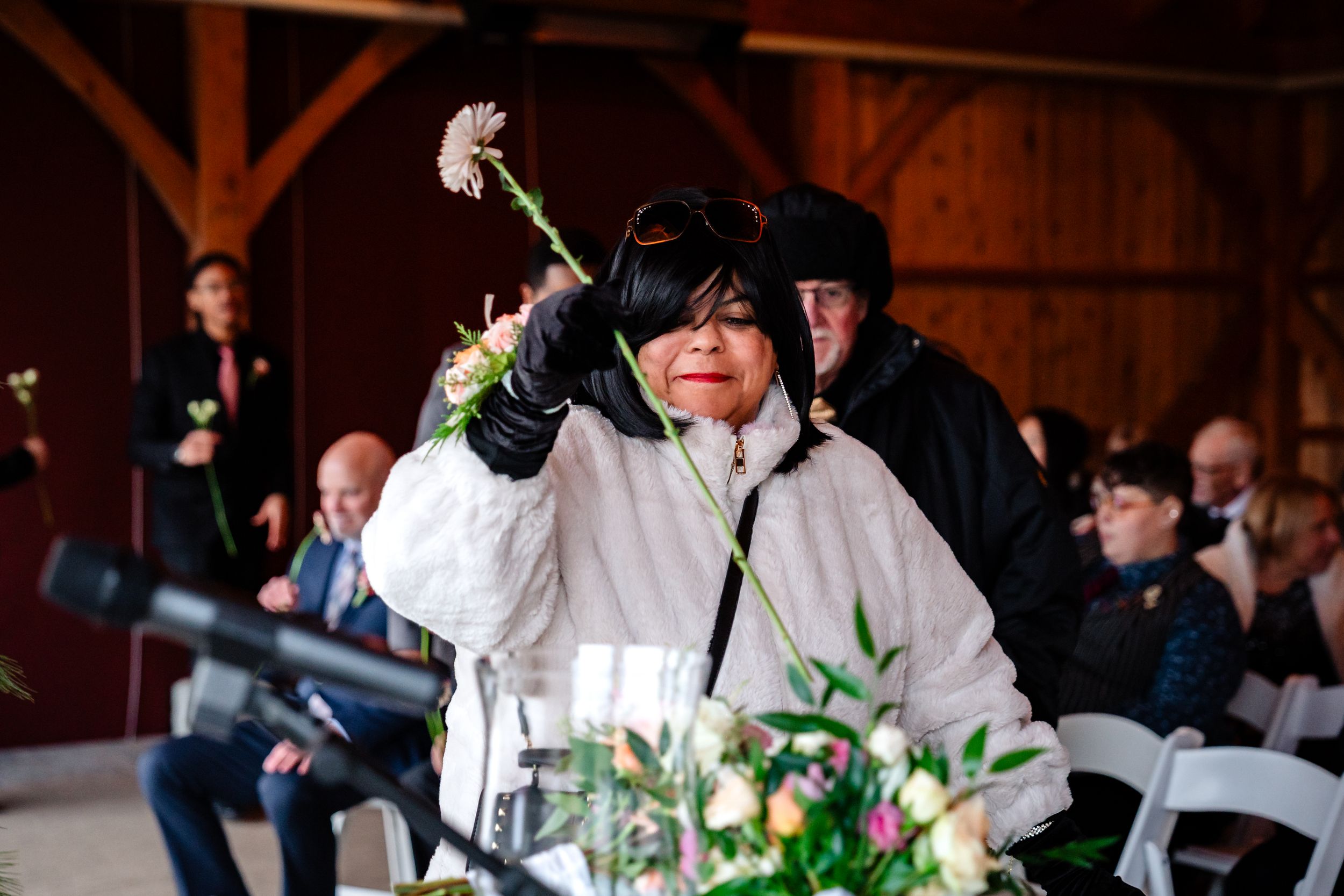 Wedding guests enjoying a celebration in a rustic wooden barn venue with white chairs.