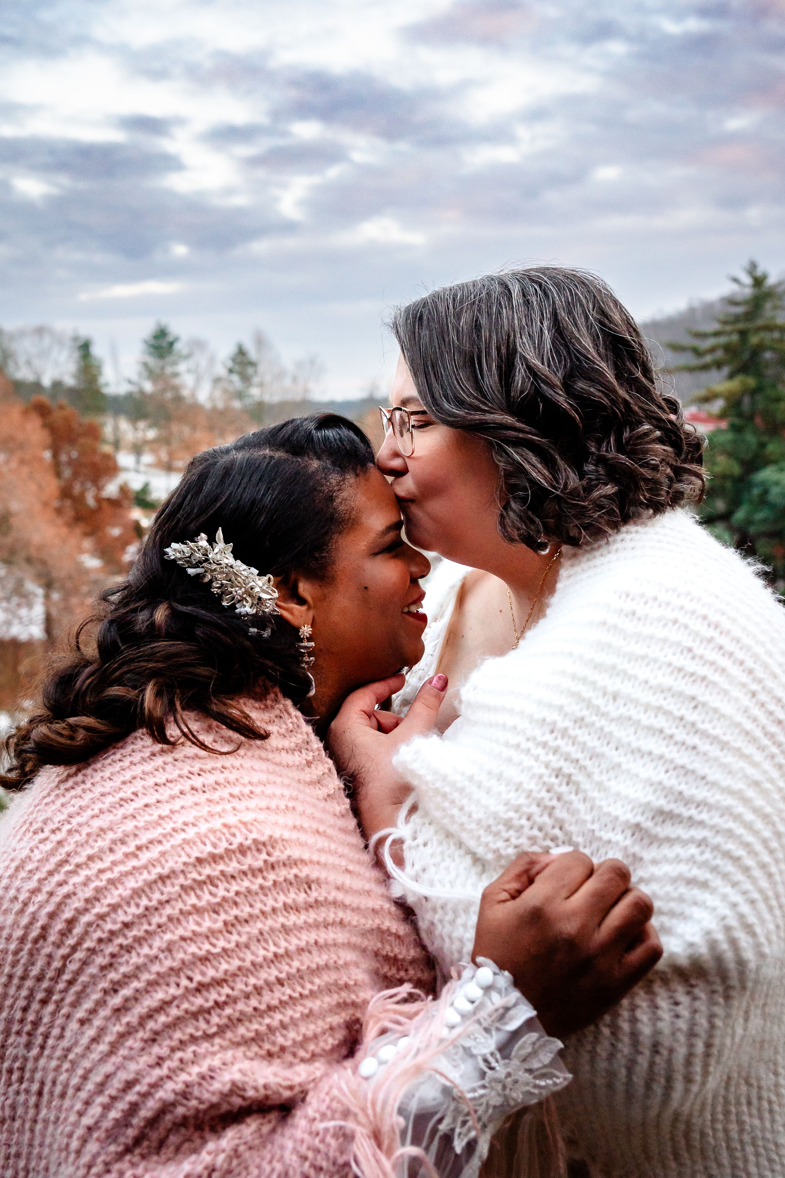 Two people share an intimate moment wrapped in cozy sweaters against an autumn mountain backdrop.