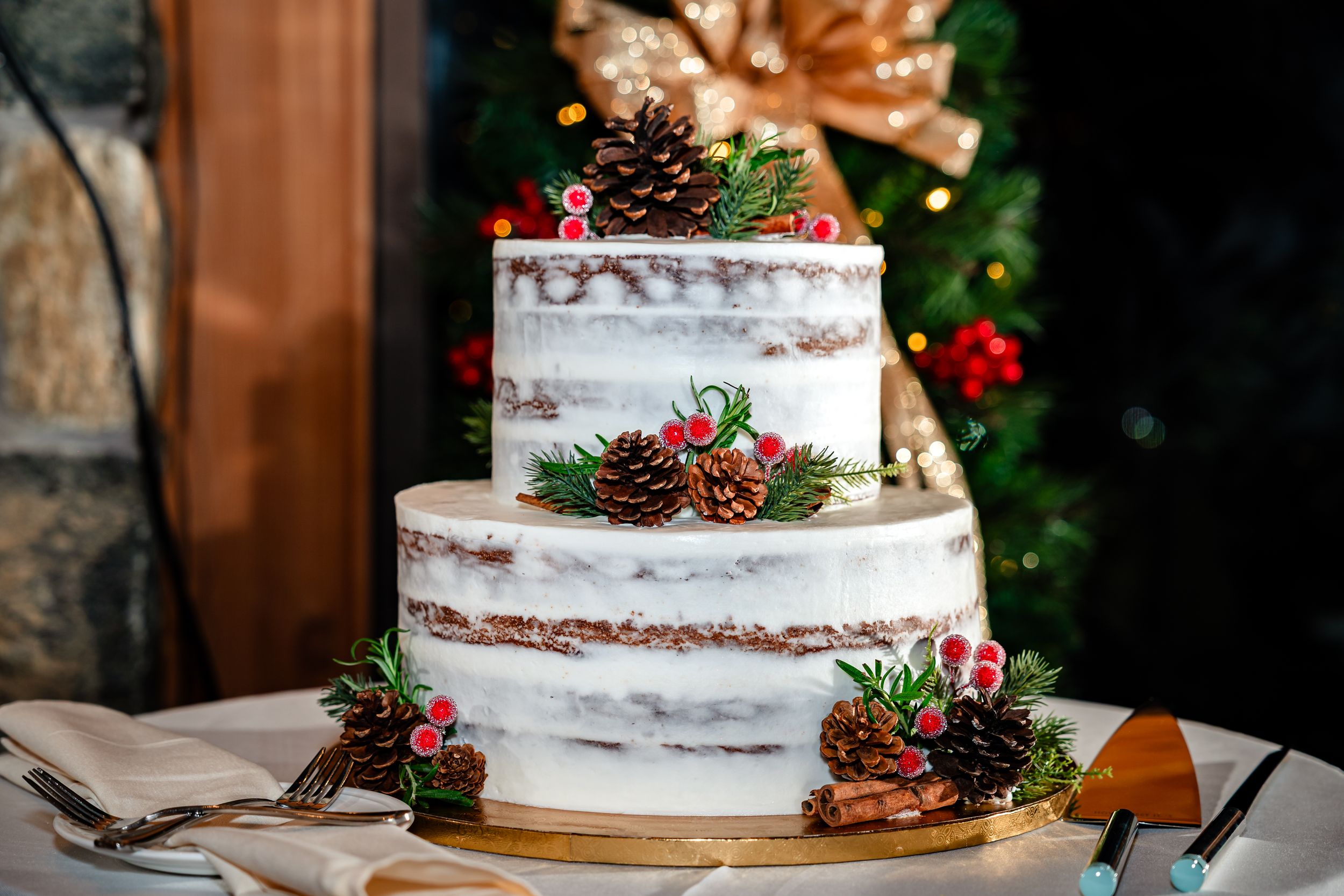 Semi-naked wedding cake decorated with winter greenery and pinecones on a rustic wooden display.