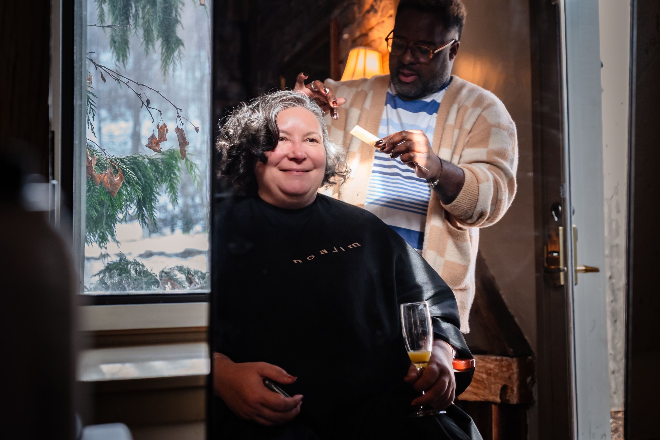 A hairstyling session takes place by a window on a snowy day.