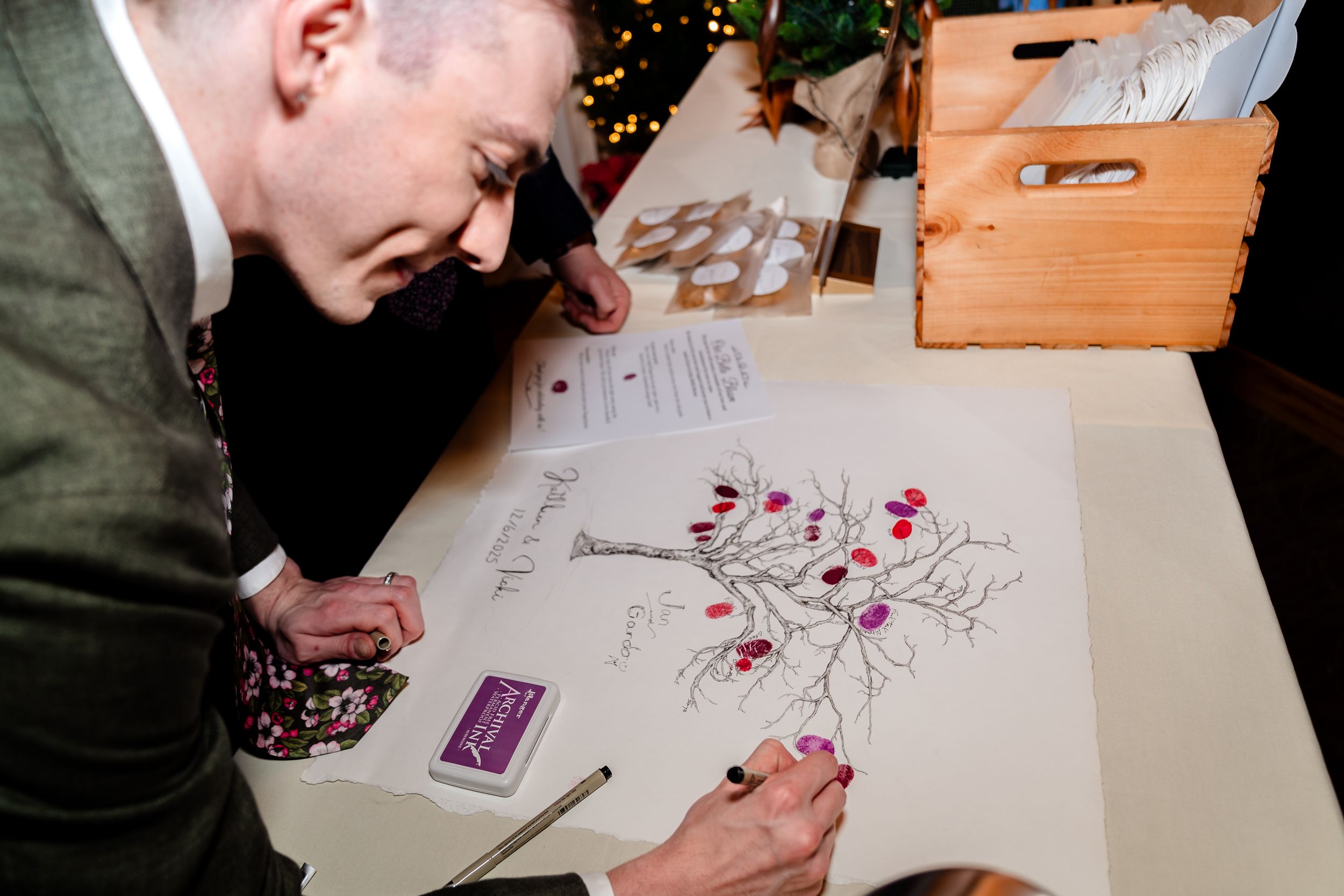 Wedding guests signing the guestbook at a wooden table with pens and decorative elements.