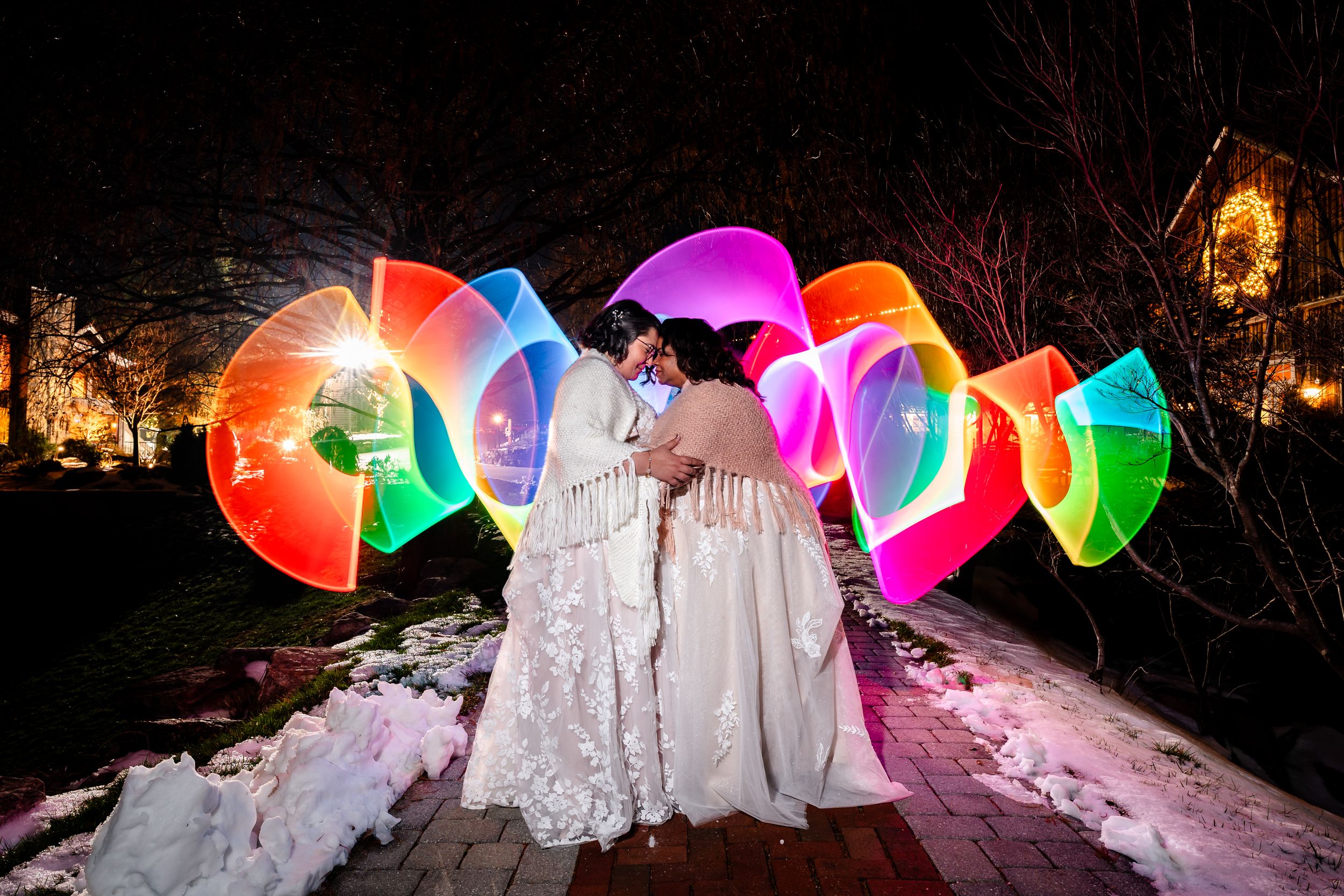 Colorful illuminated umbrellas create a magical light display against snow-covered trees at night.