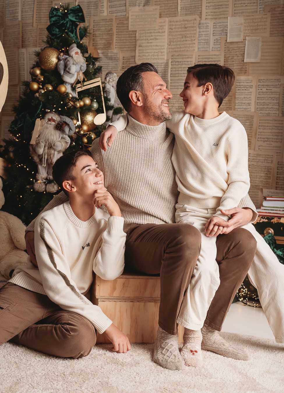 Cozy holiday scene with people in cream sweaters sitting together by a decorated Christmas tree.