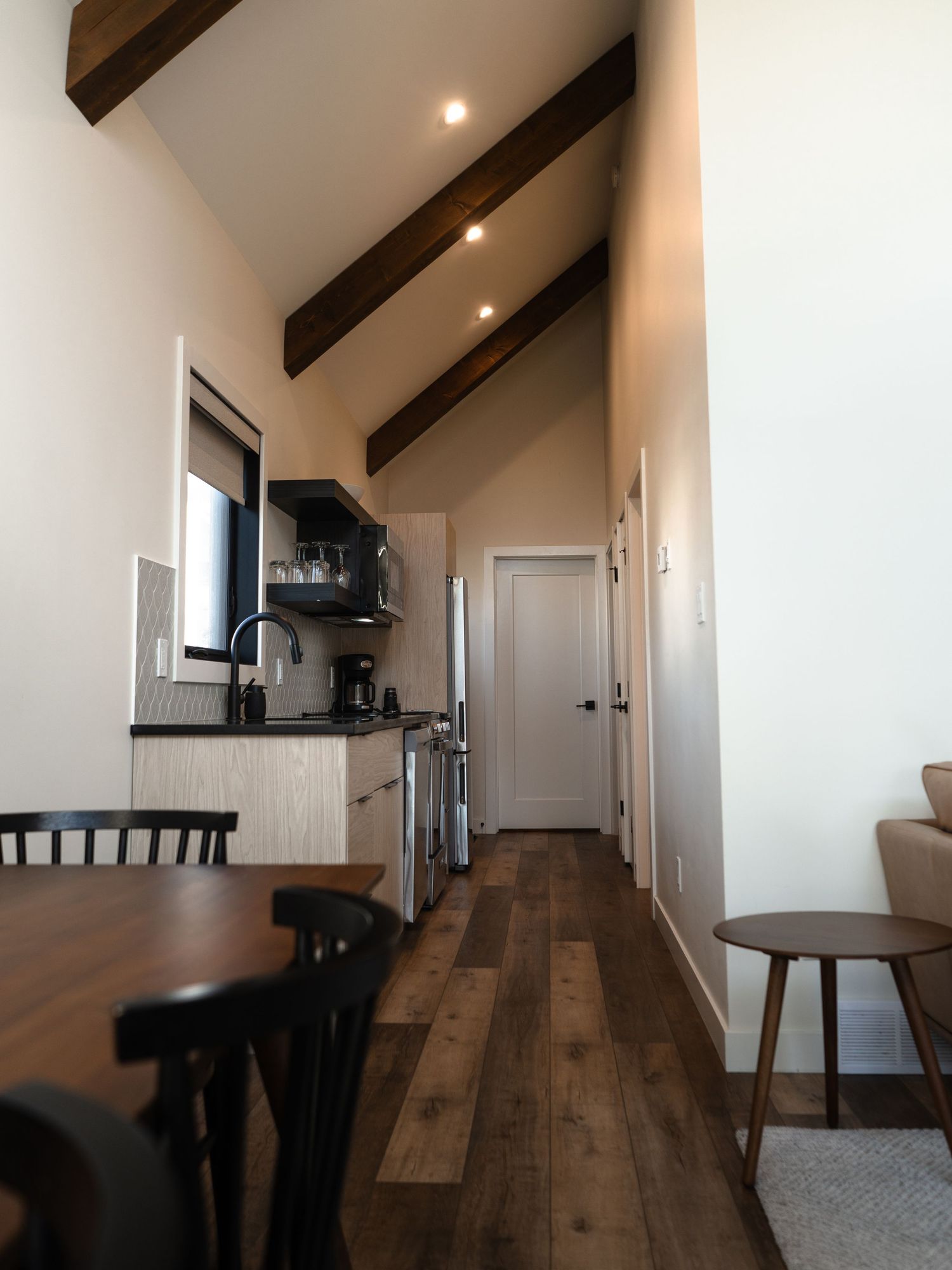 Modern cabin interior with exposed wooden beams, hardwood floors and white walls in galley-style layout.