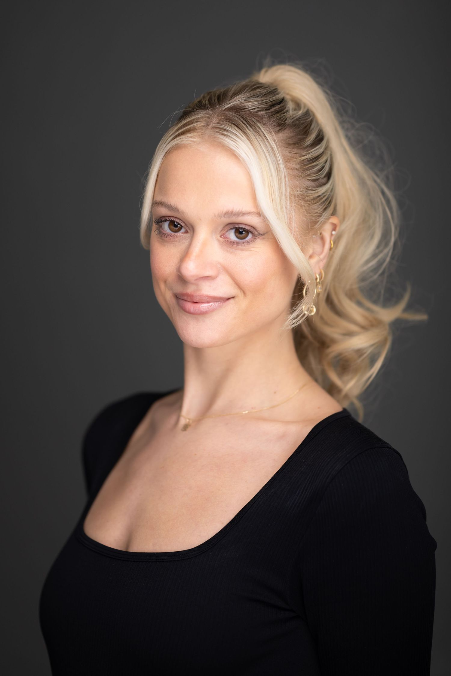 Portrait of person with blonde hair wearing black top against dark studio background.