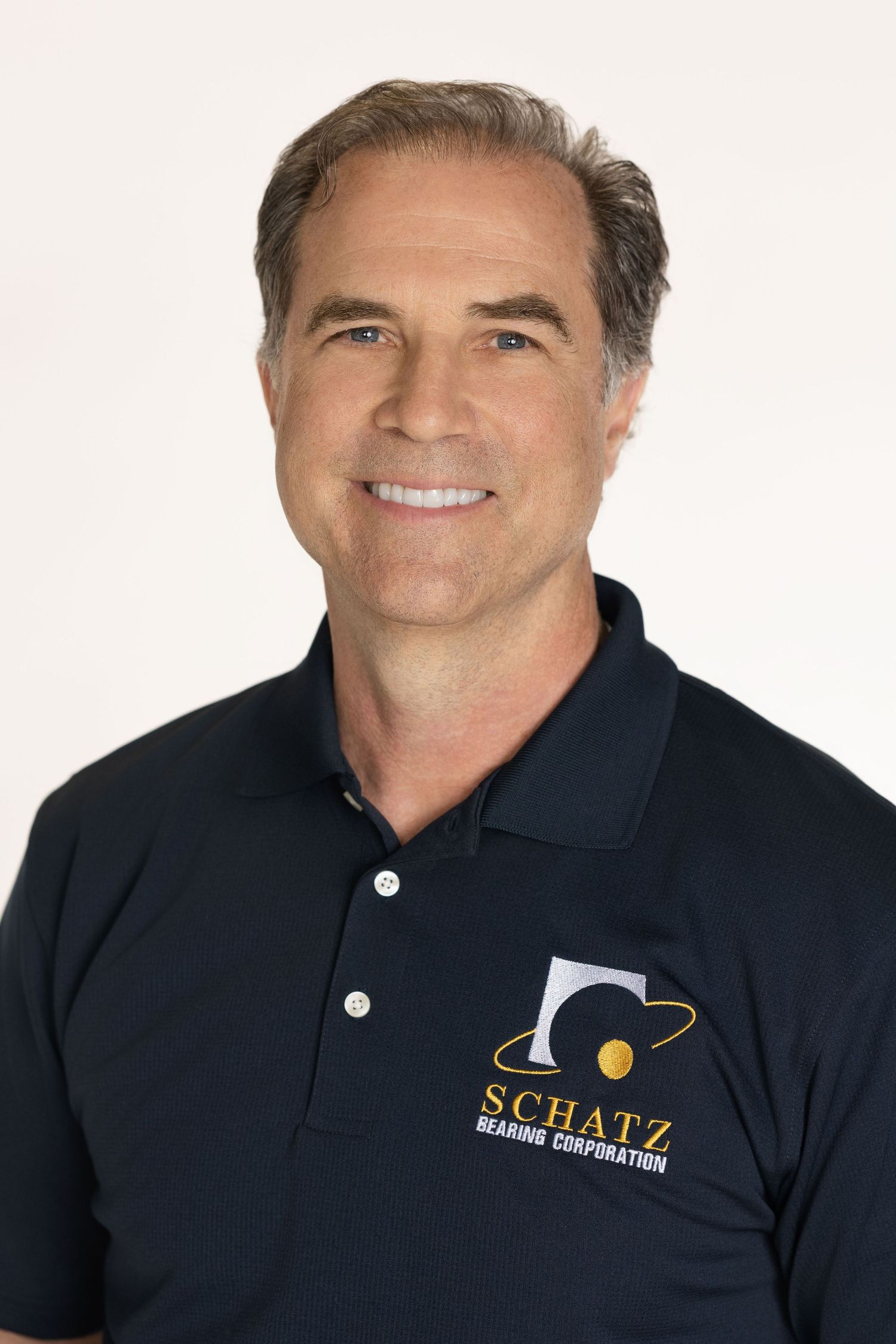 Professional headshot of person wearing navy polo shirt with company logo against white background.