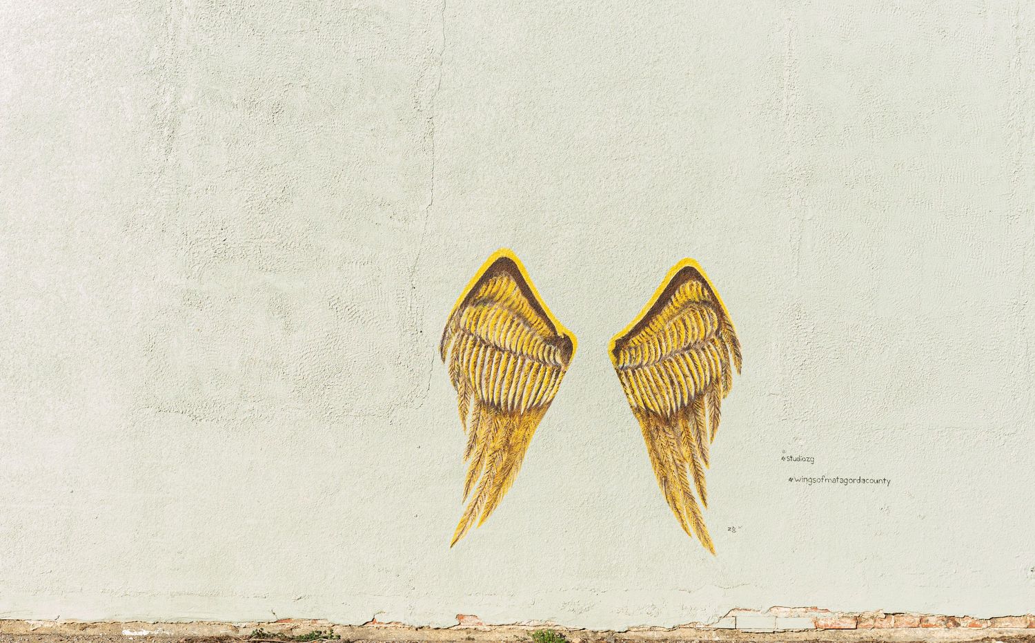Golden wings painted on white outdoor wall. Bay city branding session.