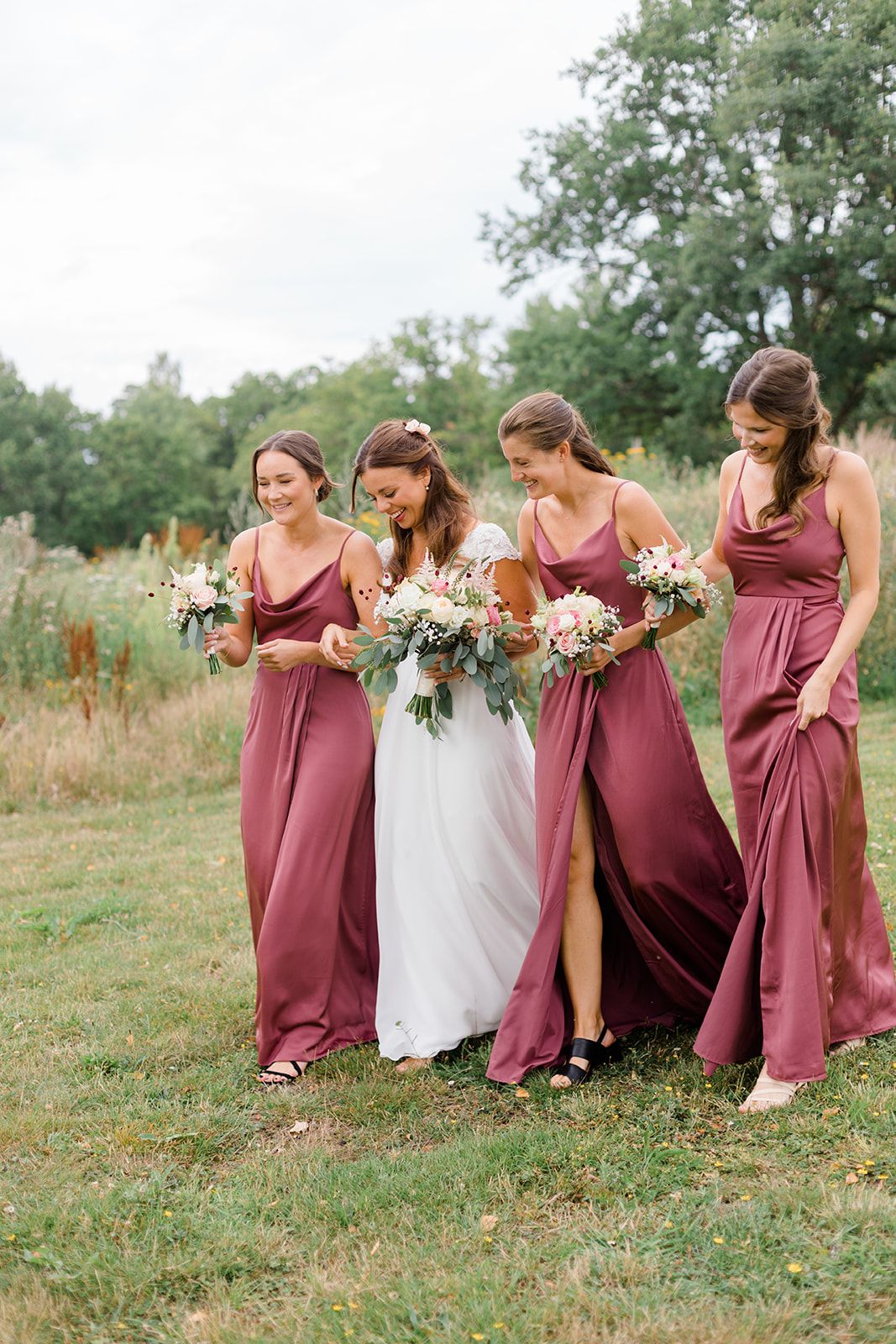 A sequence of bridesmaids in burgundy dresses playfully posing in a grassy field at a wedding photoshoot.