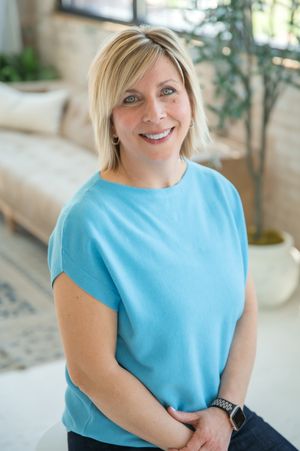 Person wearing light blue top smiles warmly while sitting in bright indoor setting with natural lighting.