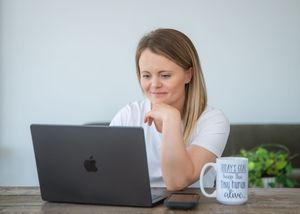 Woman looking tired and stressed while working at laptop with coffee mug on desk.