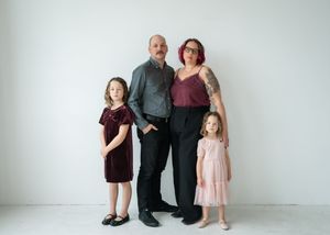 Family wearing coordinating outfits poses together against a white studio backdrop.