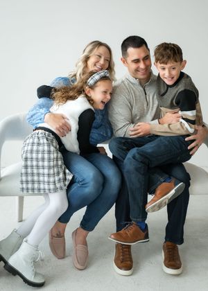 A joyful family sharing laughter while sitting close together on a white couch against a light background.