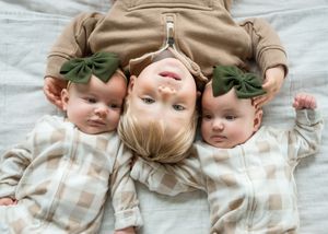 Baby wearing green bow headband lies on white blanket in progressive monthly milestone photo series.