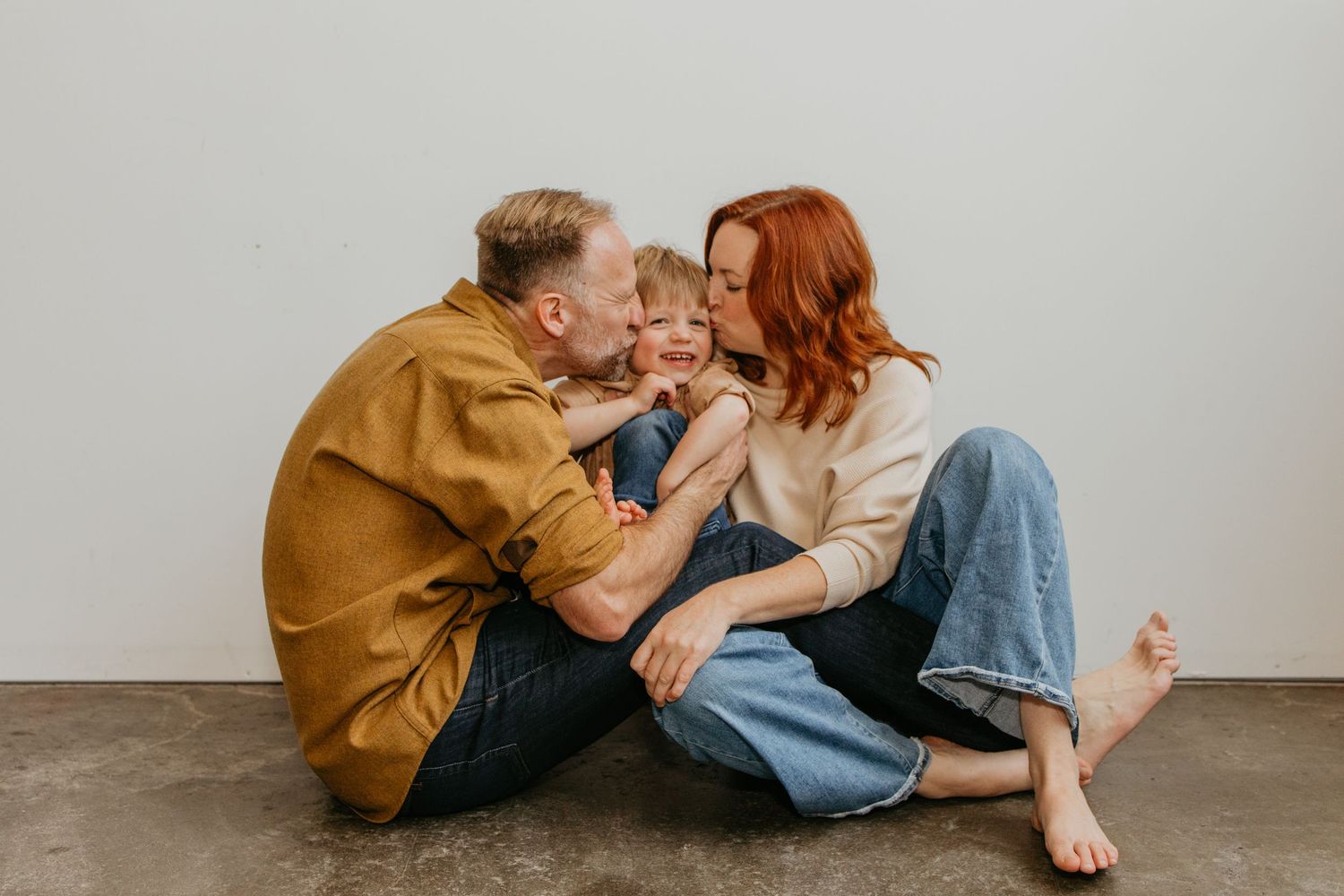 A couple in casual clothing sits together on a concrete floor sharing an intimate moment.