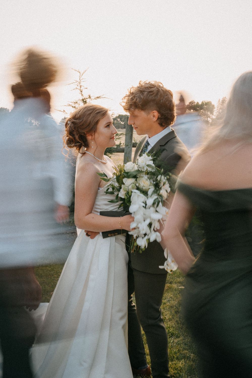 Artistic wedding photo showing blurred motion of guests surrounding a couple during an outdoor celebration.