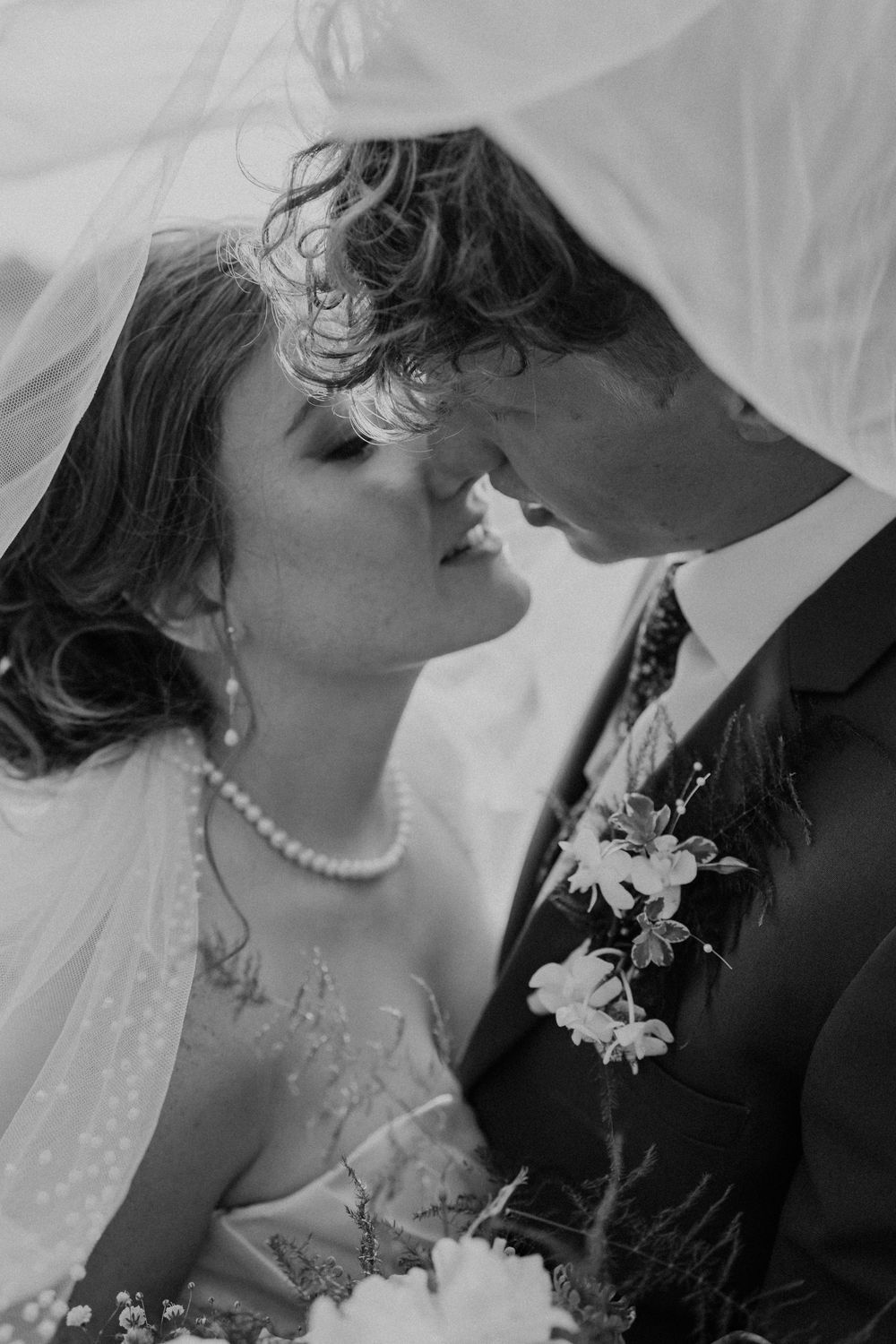 Romantic black and white wedding portrait showing a couple in an intimate close-up moment under a veil.