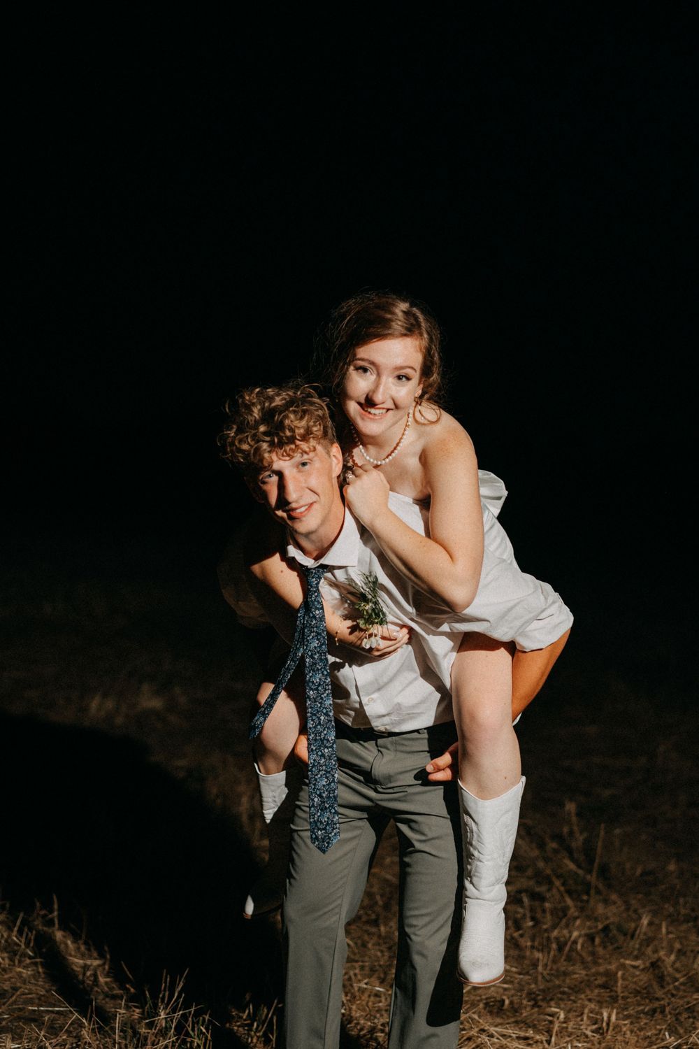 Playful wedding couple poses in dramatic lighting against dark background.