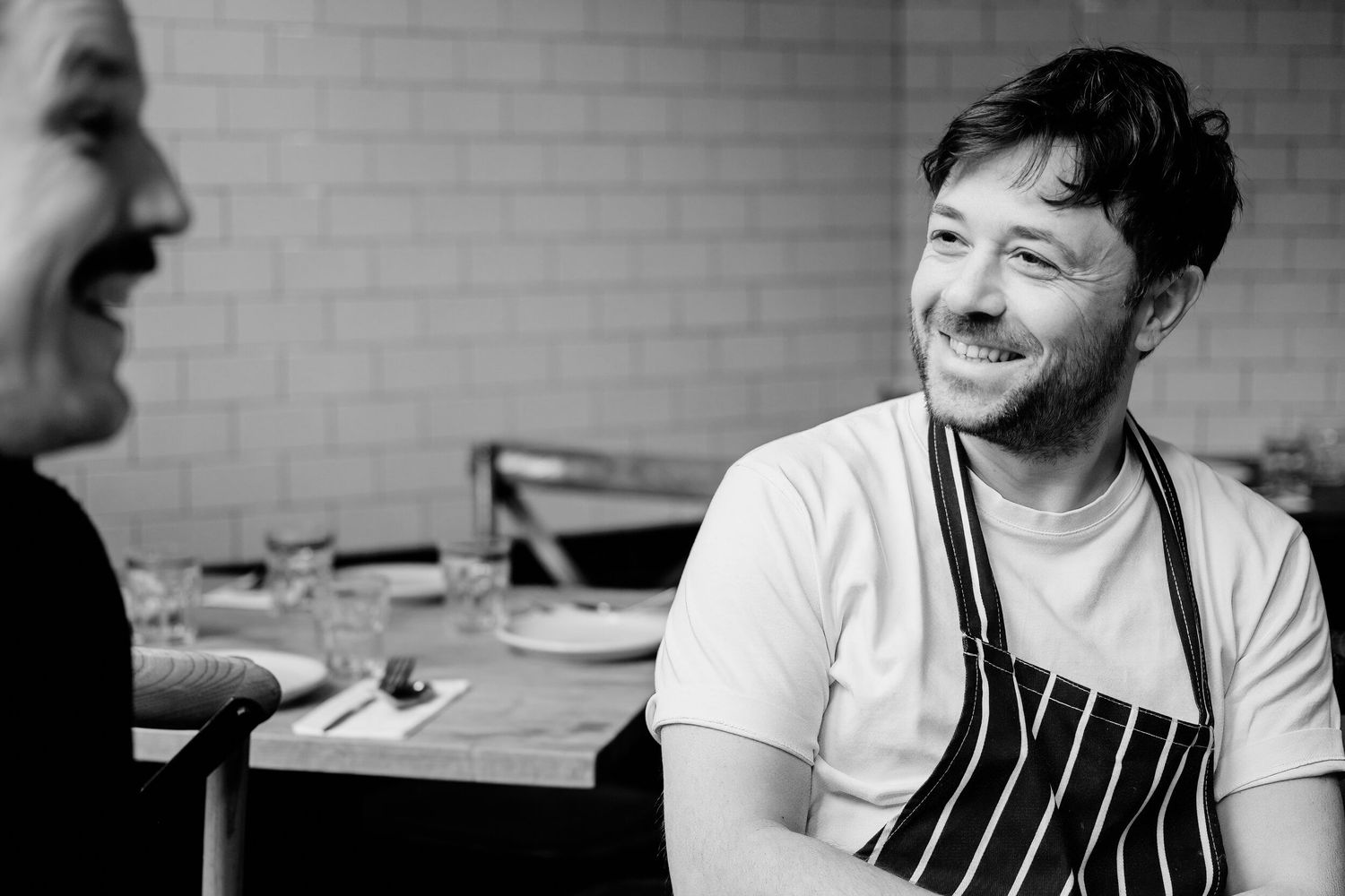 A black and white collage of chefs in kitchen settings wearing aprons and striped uniforms.