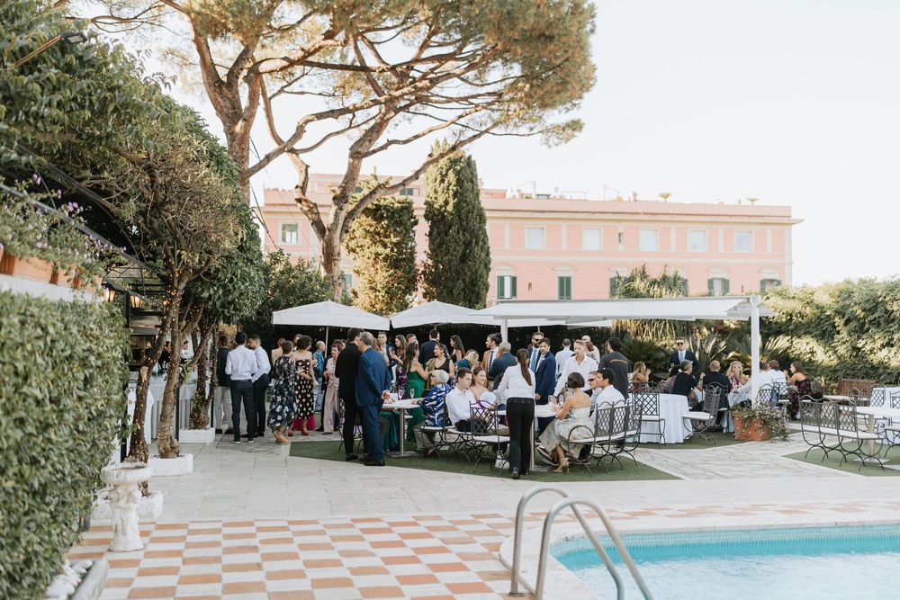 Outdoor wedding reception setup with tables and chairs arranged under tall pine trees at sunset.
