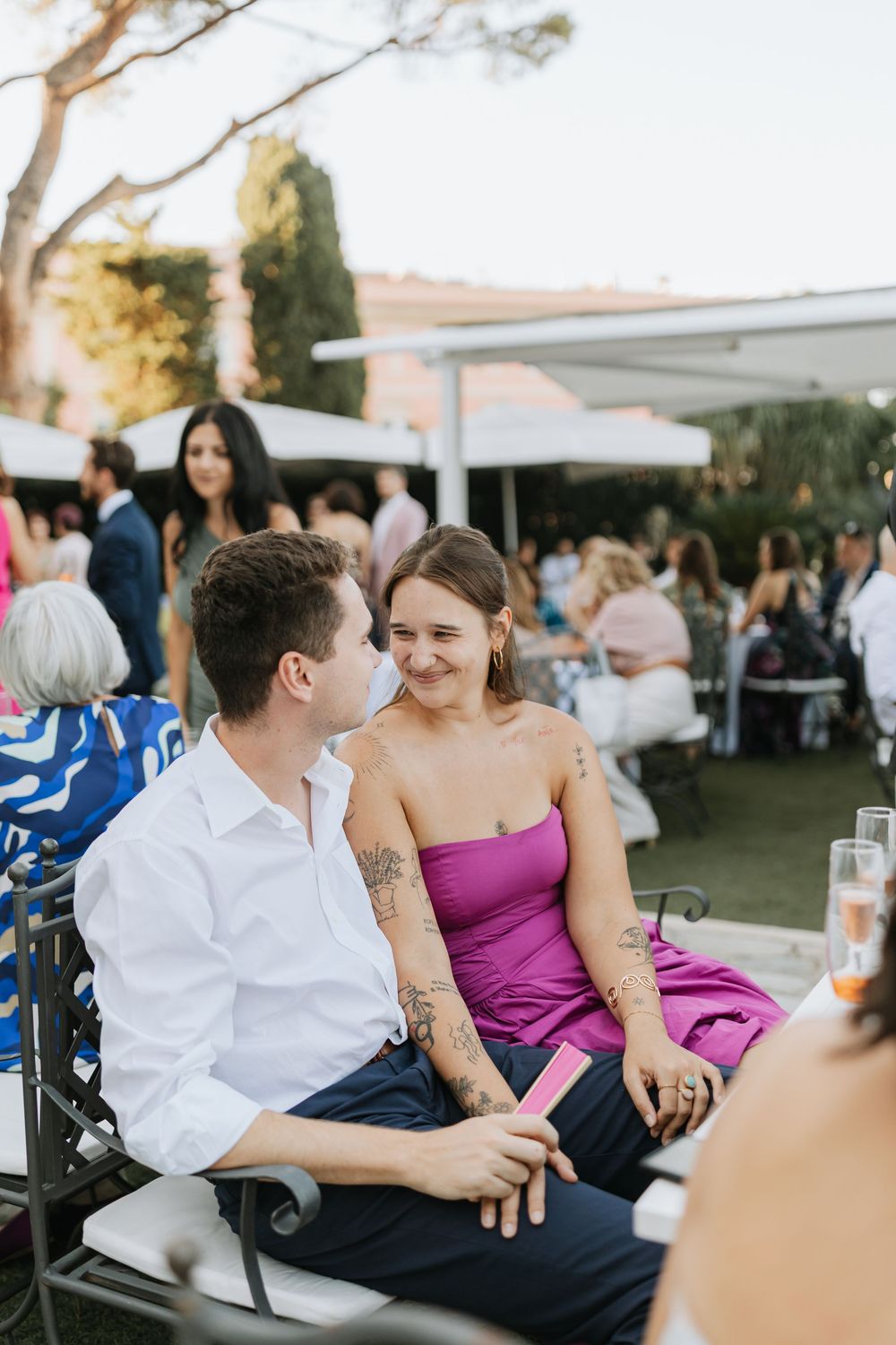 Wedding guests in formal attire socialize at outdoor reception during golden hour.