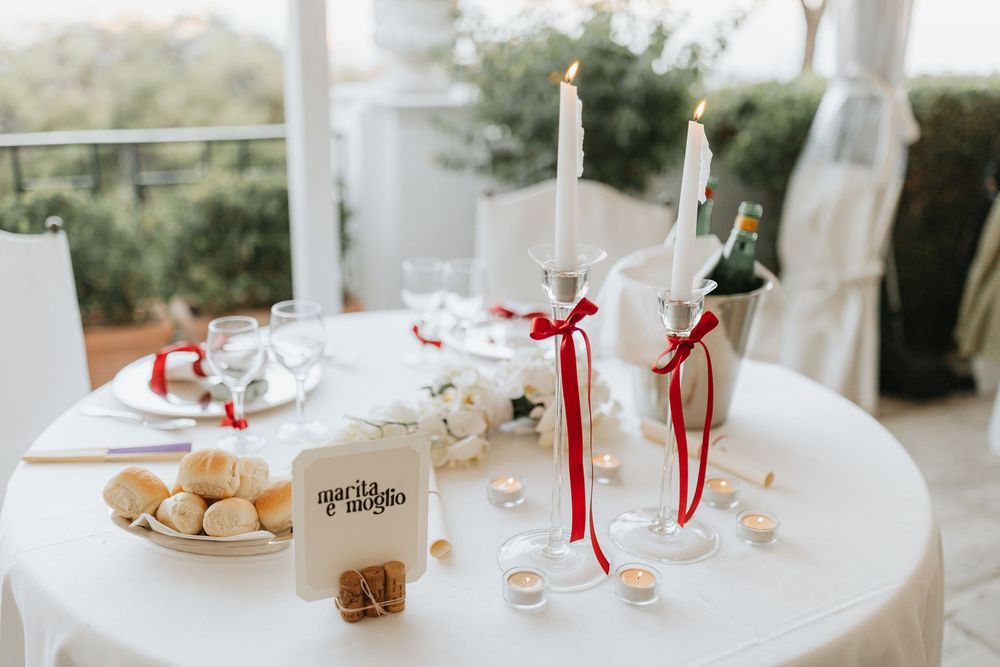 A long white banquet table decorated with elegant place settings, floral arrangements, and red ribbon accents.