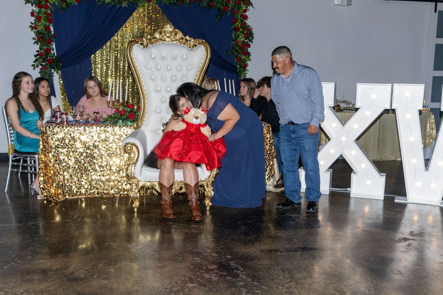 A group of people dancing at a party with a gold sequin backdrop and festive decorations.