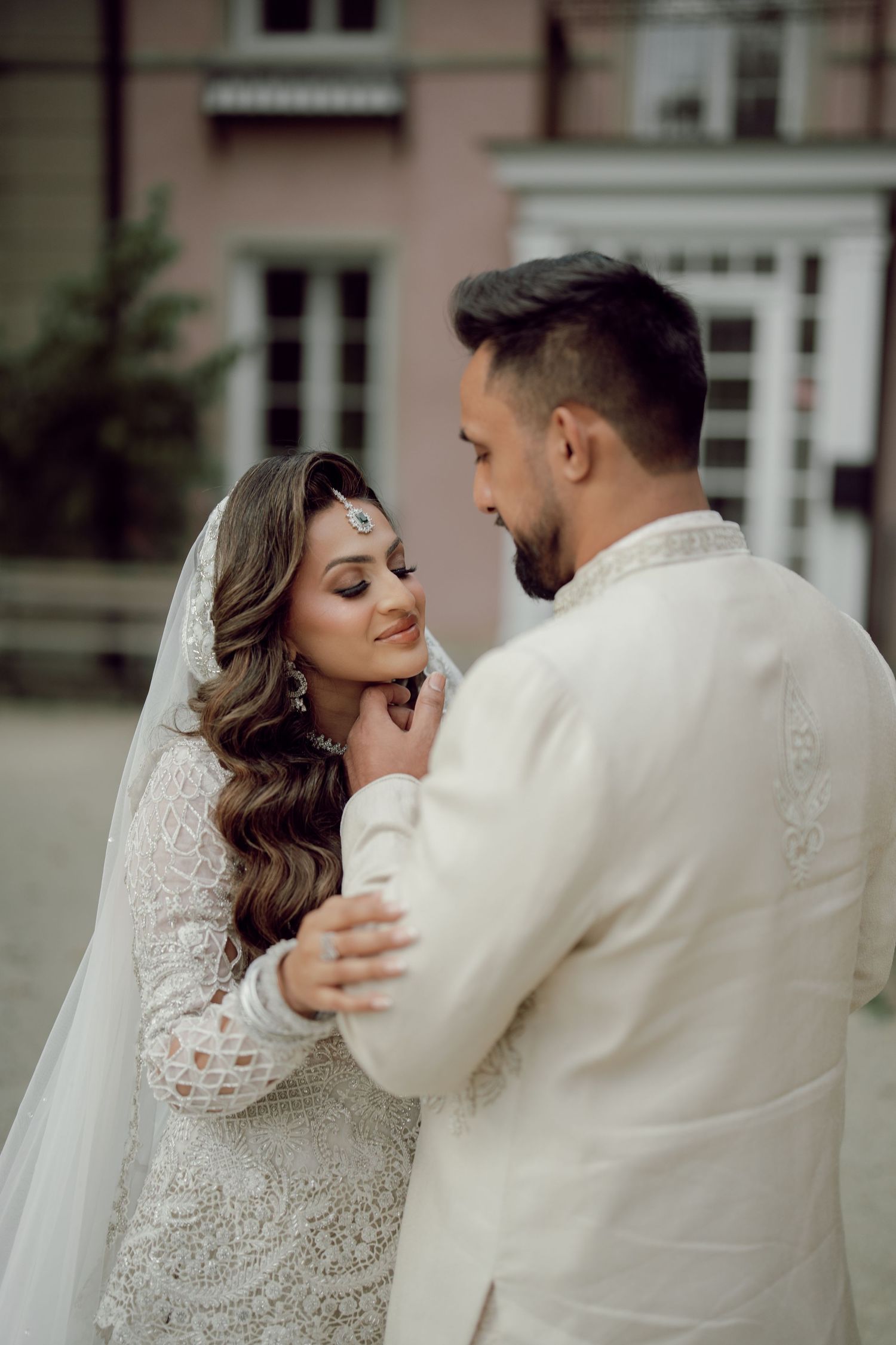 South Asian bride and groom in white traditional attire share intimate moment under vibrant autumn foliage.