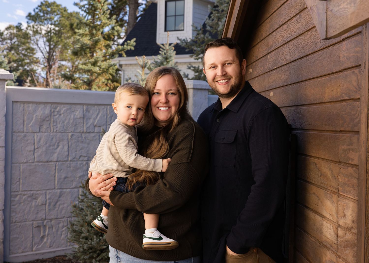 Family poses together against rustic wood paneled wall during outdoor photo session.