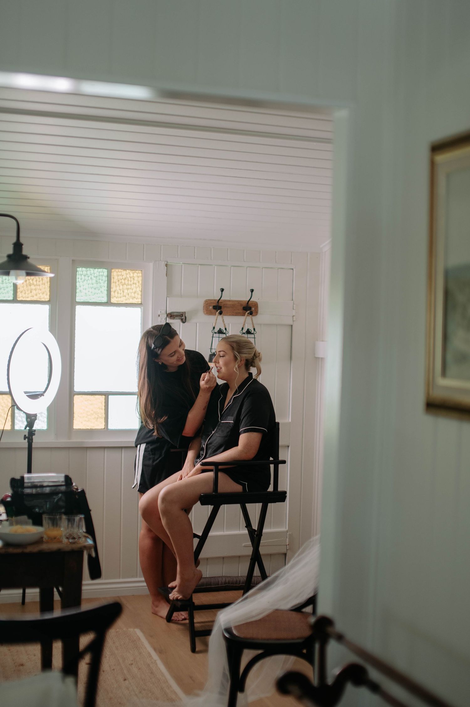 Two people sit together in a bright room with white wainscoting and natural light streaming through windows.